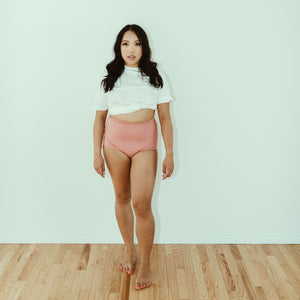 Woman posing in clay (pink) organic cotton high rise underwear, front view.