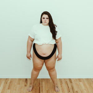 Plus size woman posing in onyx (black) cheeky organic cotton underwear, front view.